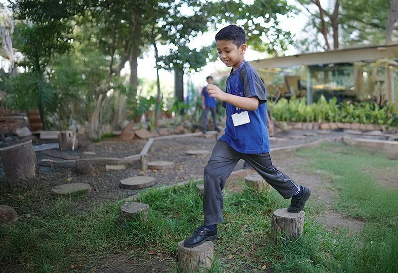 Young Student Stepping Across Wooden Log Stumps in School Outdoor Play Area